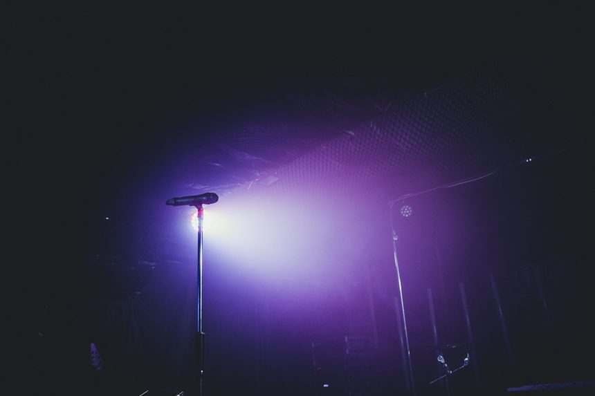 Microfone em um palco vazio iluminado por luzes roxas, preparado para uma apresentação musical.