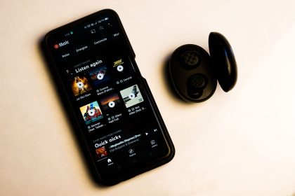 Smartphone exibindo uma interface de aplicativo de música ao lado de fones de ouvido sem fio sobre fundo neutro