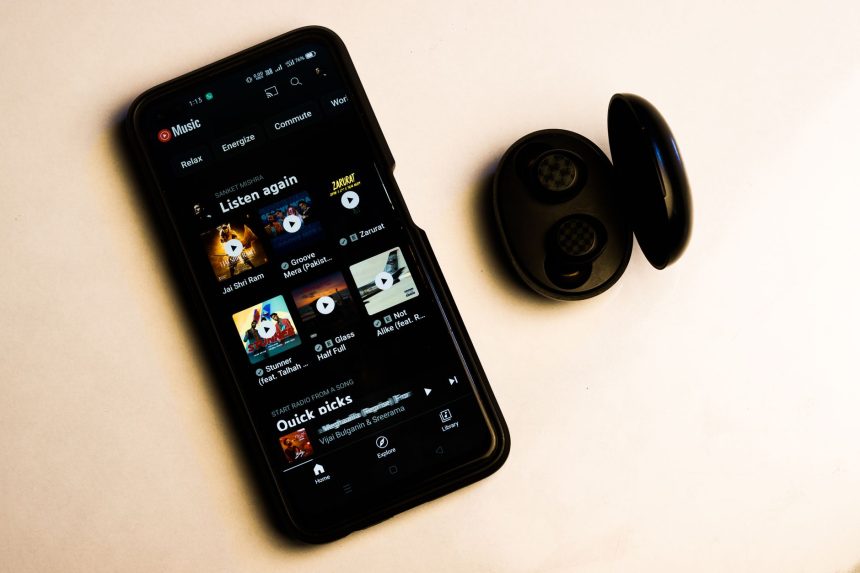 Smartphone exibindo uma interface de aplicativo de música ao lado de fones de ouvido sem fio sobre fundo neutro