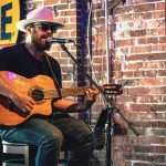 Músico toca violão em um bar de Nashville, diante de um microfone.