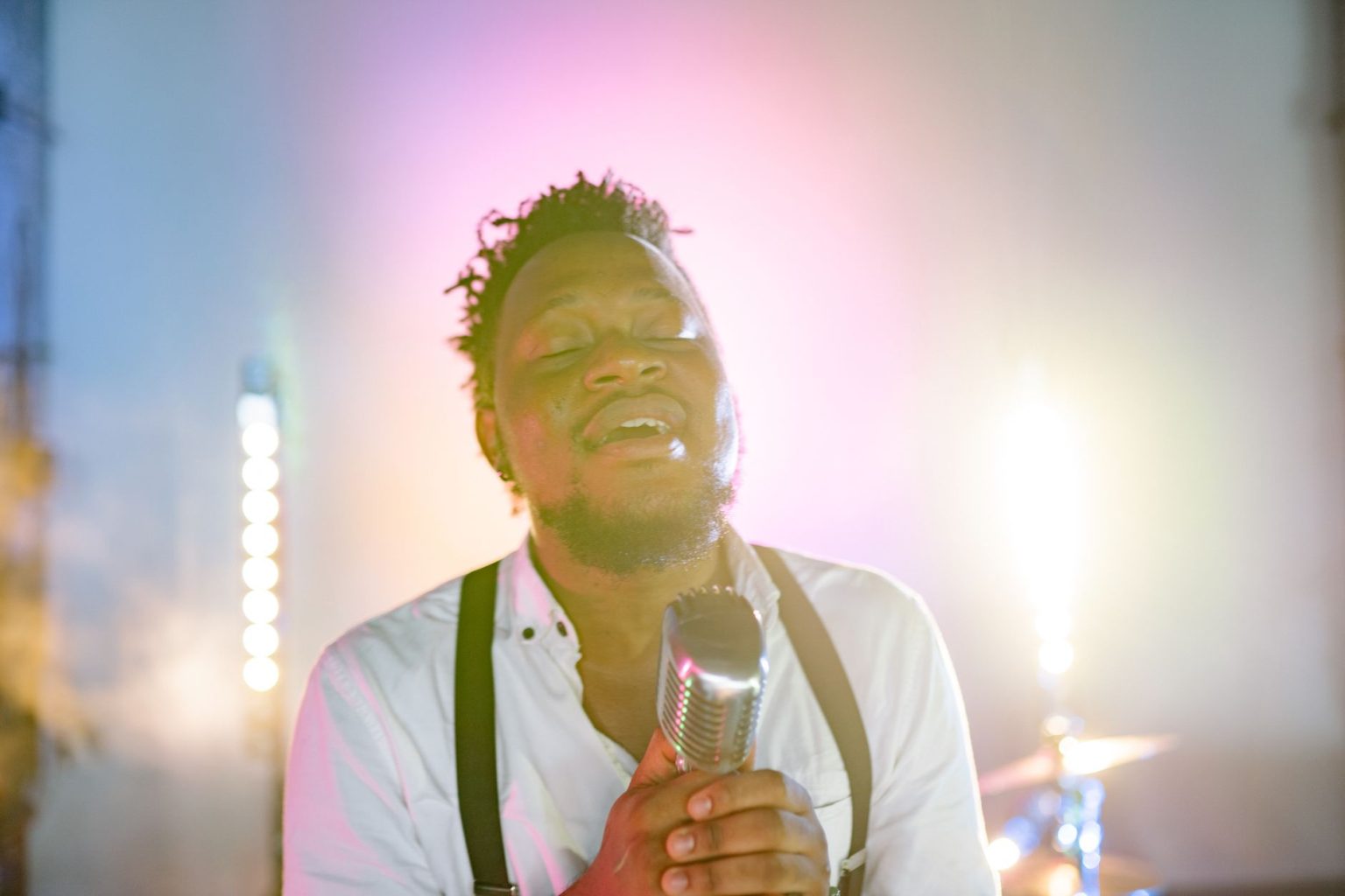 Cantor negro se apresenta ao microfone em um palco com estética retrô.