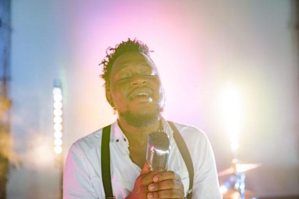 Cantor negro se apresenta ao microfone em um palco com estética retrô.