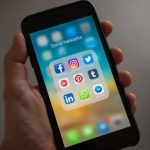Mão segurando um smartphone com ícones de aplicativos de redes sociais na tela