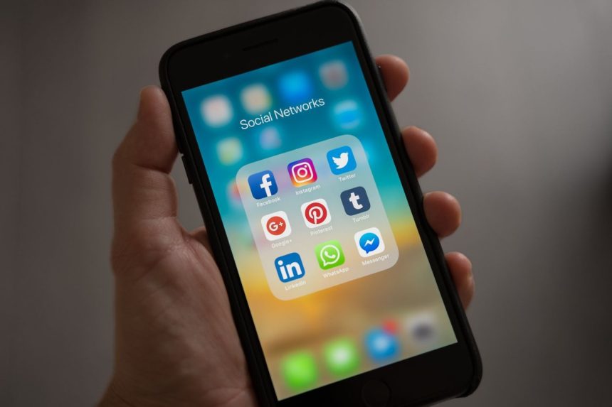 Mão segurando um smartphone com ícones de aplicativos de redes sociais na tela