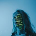 Mulher com luzes em formato de código binário projetadas sobre o rosto, em uma composição que remete à tecnologia e à segurança digital.