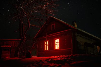 Casa assombrada com janelas iluminadas em vermelho sob um céu estrelado